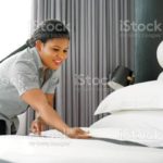 Maid making bed in hotel room. Staff Maid Making Bed. African housekeeper making bed.